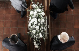 Funeral, family coffin and church above for death, grief or burial service with solidarity. Group, pallbearers and people together with casket for respect, farewell or sad in mourning, mass or loss
