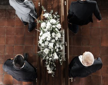 Funeral, family coffin and church above for death, grief or burial service with solidarity. Group, pallbearers and people together with casket for respect, farewell or sad in mourning, mass or loss