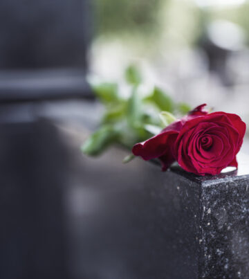 Rose on tombstone. Red rose on grave. Love - loss. Flower on memorial stone close up. Tragedy and sorrow for the loss of a loved one. Memory. Gravestone with withered rose